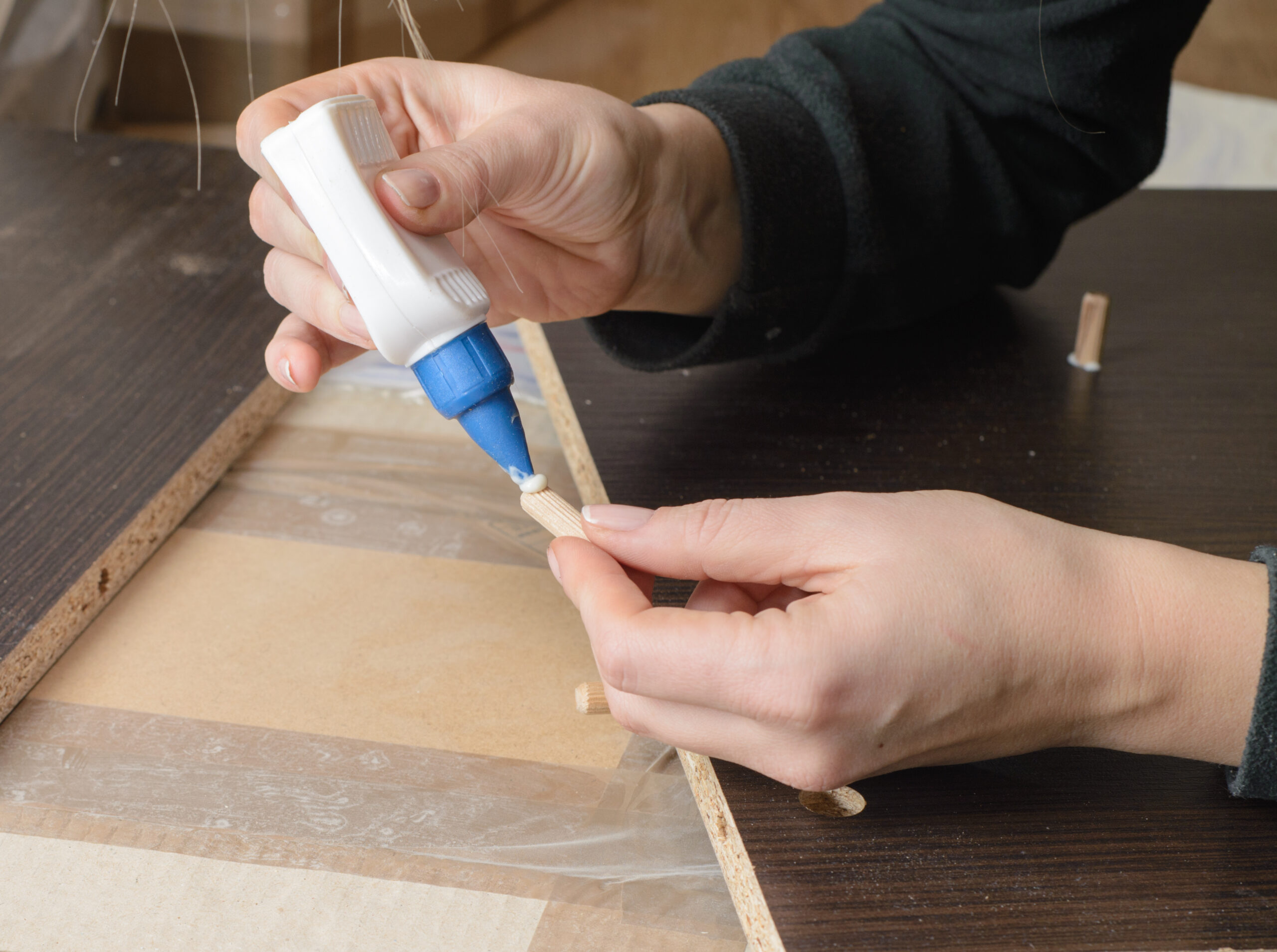 Man dressed in workers' overall assembling furniture sitting on the floor and glues furniture details